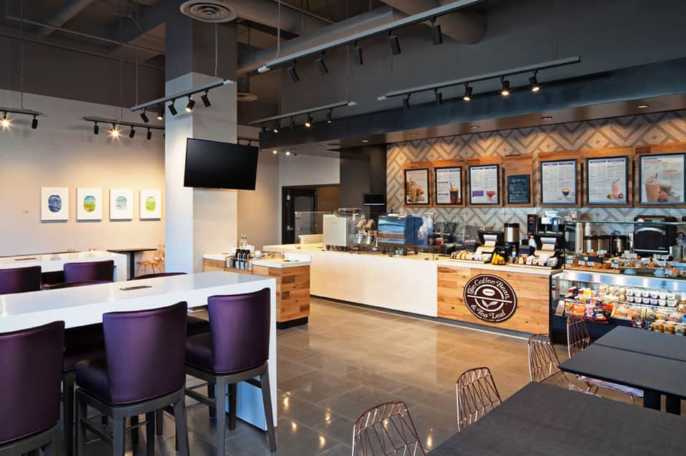 Modern coffee shop interior with purple seating, wooden counter, menu boards, and track lighting