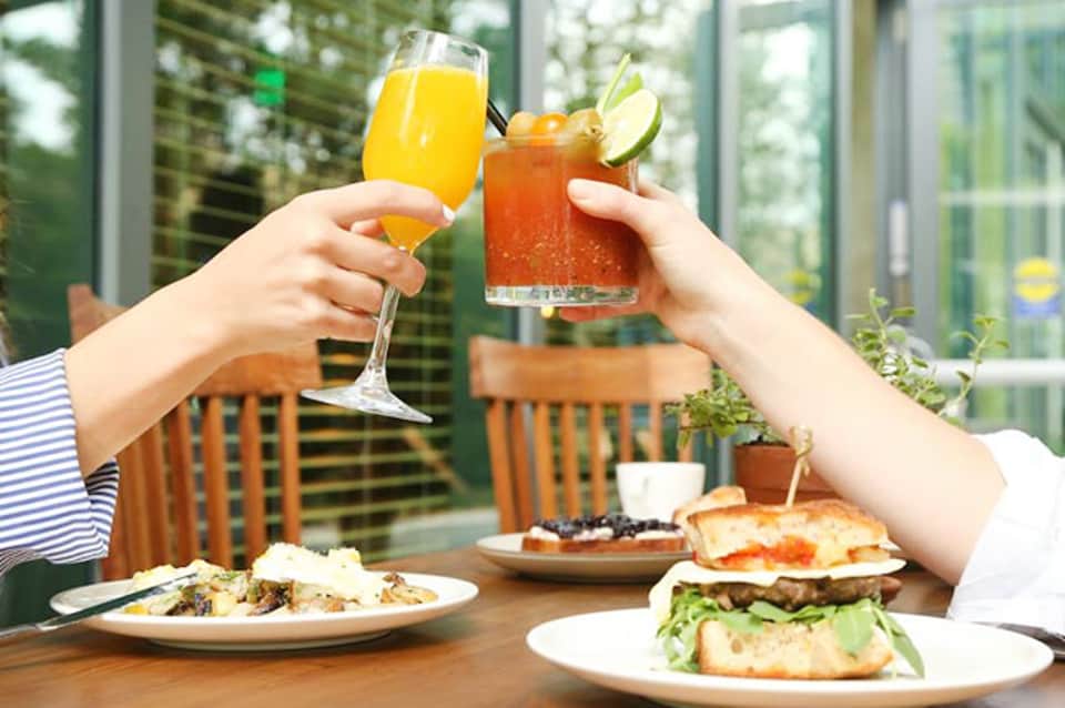 Two people toasting drinks at outdoor dining table with burgers and salads
