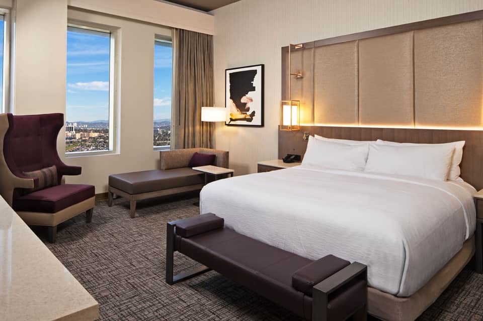 Luxury hotel bedroom with king bed, city view windows, modern furnishings, and contemporary artwork
