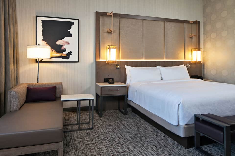 Modern hotel bedroom with white bedding, wood headboard, and contemporary furnishings