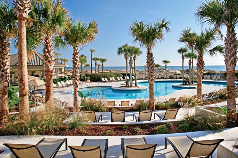 Luxury resort pool area with palm trees, lounge chairs, and ocean view at beachfront property