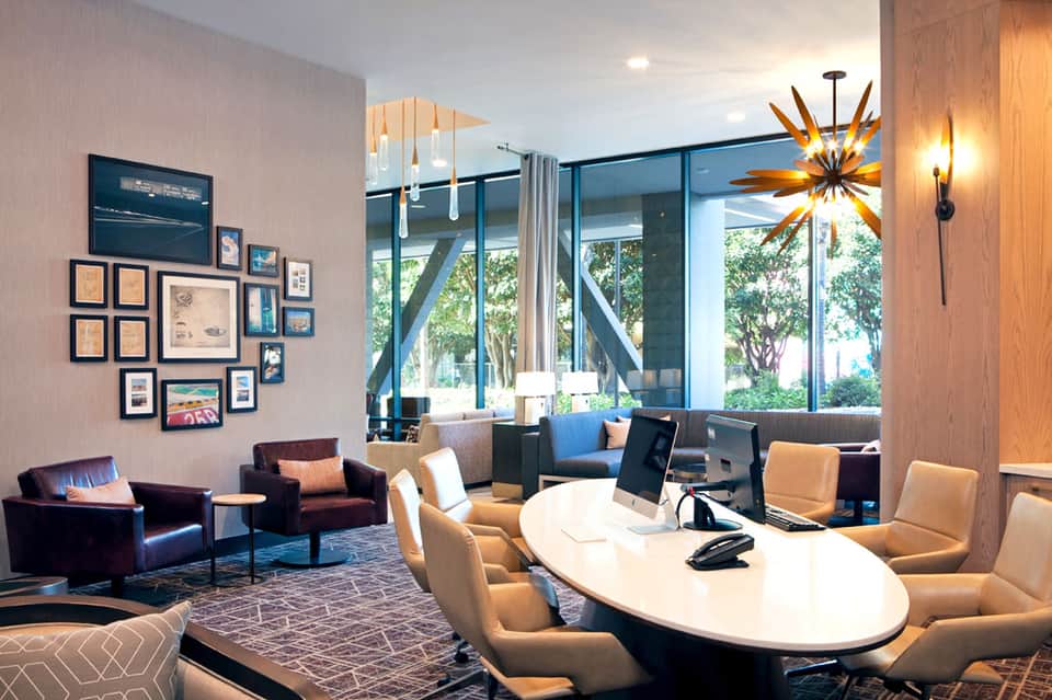 Modern hotel lobby with oval conference table, lounge seating, and floor-to-ceiling windows