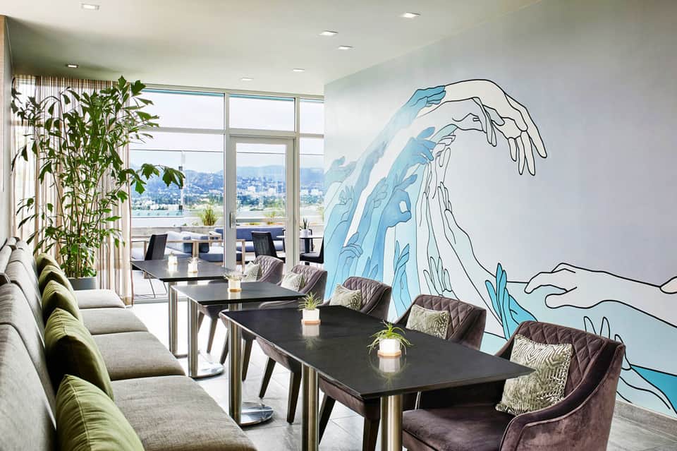 Modern lounge with blue wave mural, black tables, green accent chairs, and city views