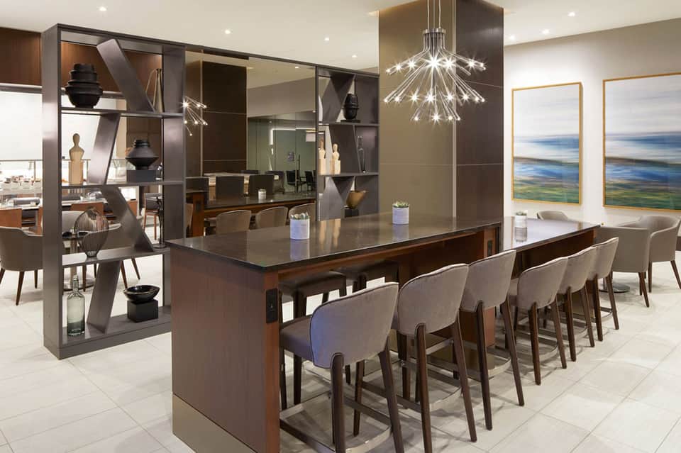 Modern kitchen and dining area with dark wood cabinetry, island seating, pendant lighting, and landscape artwork