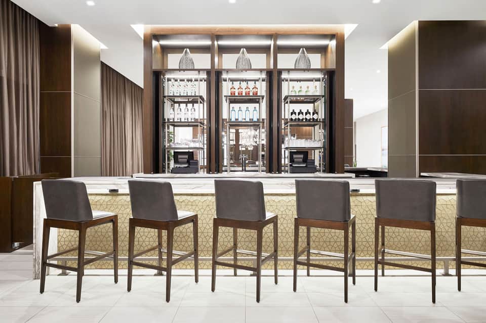 Modern bar with wooden-framed shelving, glass-front refrigerators, and upholstered bar seating