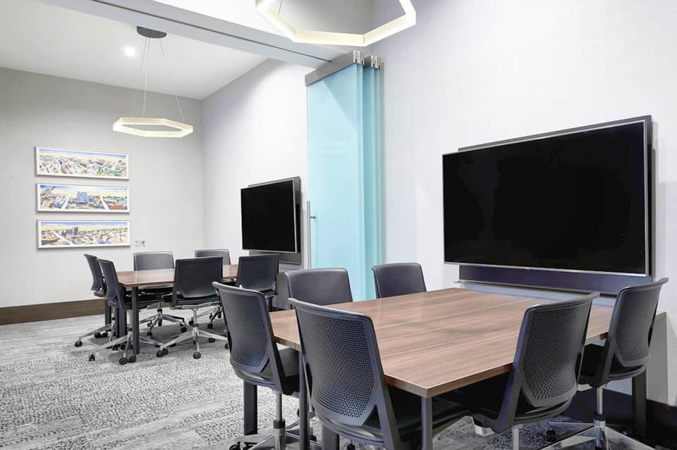 Modern conference room with wooden table, ergonomic chairs, and two large display screens