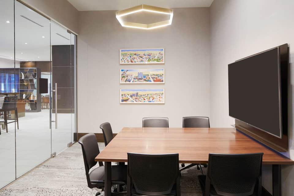 Modern conference room with wooden table, ergonomic chairs, large TV screen, and coastal artwork
