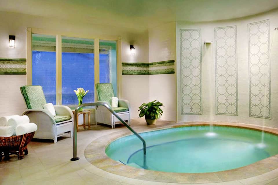 Luxury spa indoor heated pool with aquamarine water, comfortable seating, and floor-to-ceiling windows overlooking blue ocean