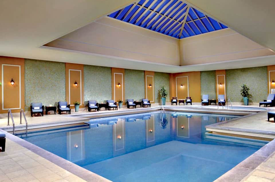 Indoor luxury pool with blue skylight ceiling, cream walls, lounge chairs, and ambient lighting