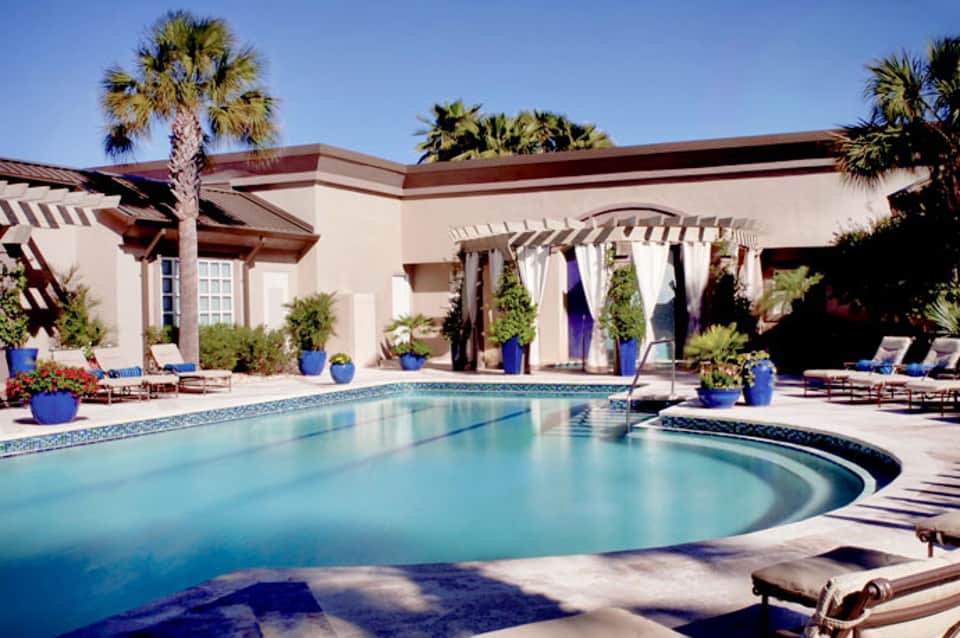 Luxury resort pool with turquoise water, palm trees, and beige building with pergolas