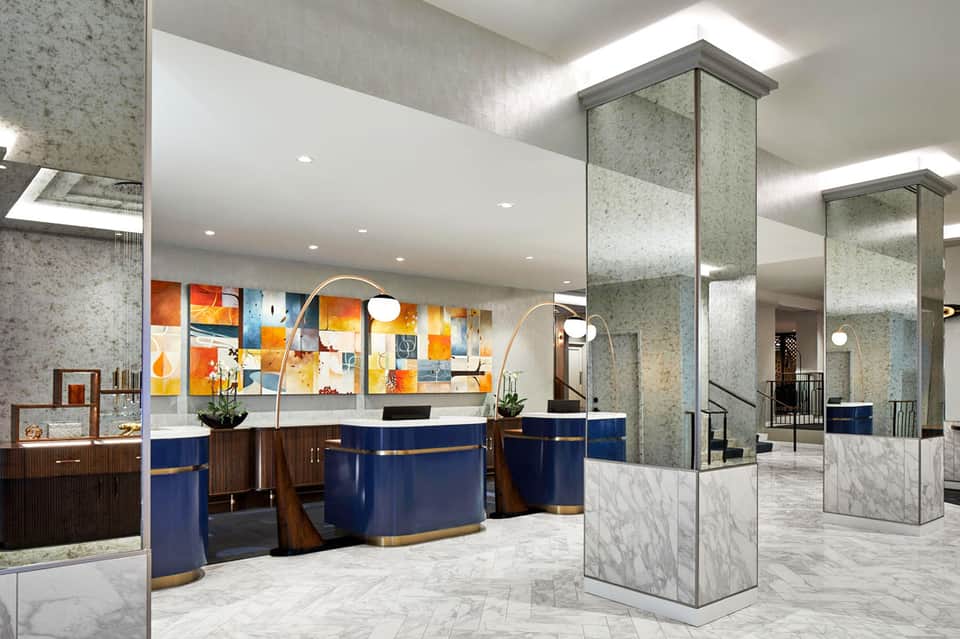 Modern hotel lobby with blue curved reception desk, marble flooring, and colorful artwork
