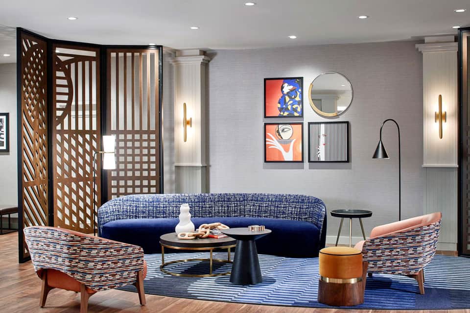 Modern hotel lounge with blue curved sofa, patterned accent chairs, decorative room divider, and abstract wall art