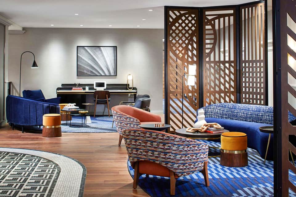 Modern hotel suite with blue armchairs, patterned accent chairs, wooden screen divider, and contemporary furnishings