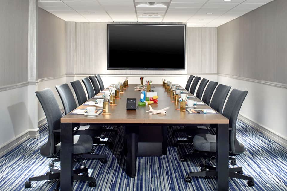 Modern boardroom with long conference table, ergonomic chairs, and large wall-mounted screen