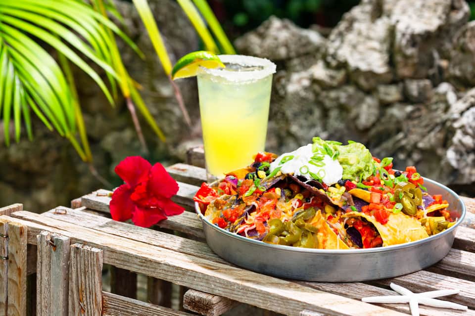 Colorful tropical salad and lime drink served on wooden deck by rocky coastline