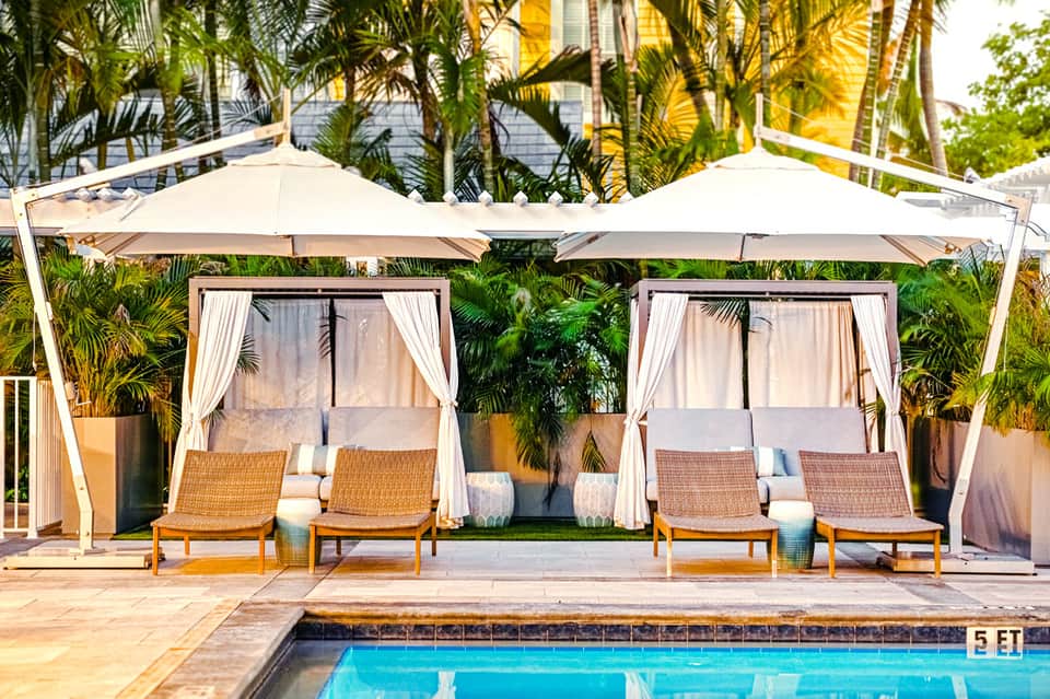 Poolside cabanas with white pergolas, cream umbrellas, and wicker loungers