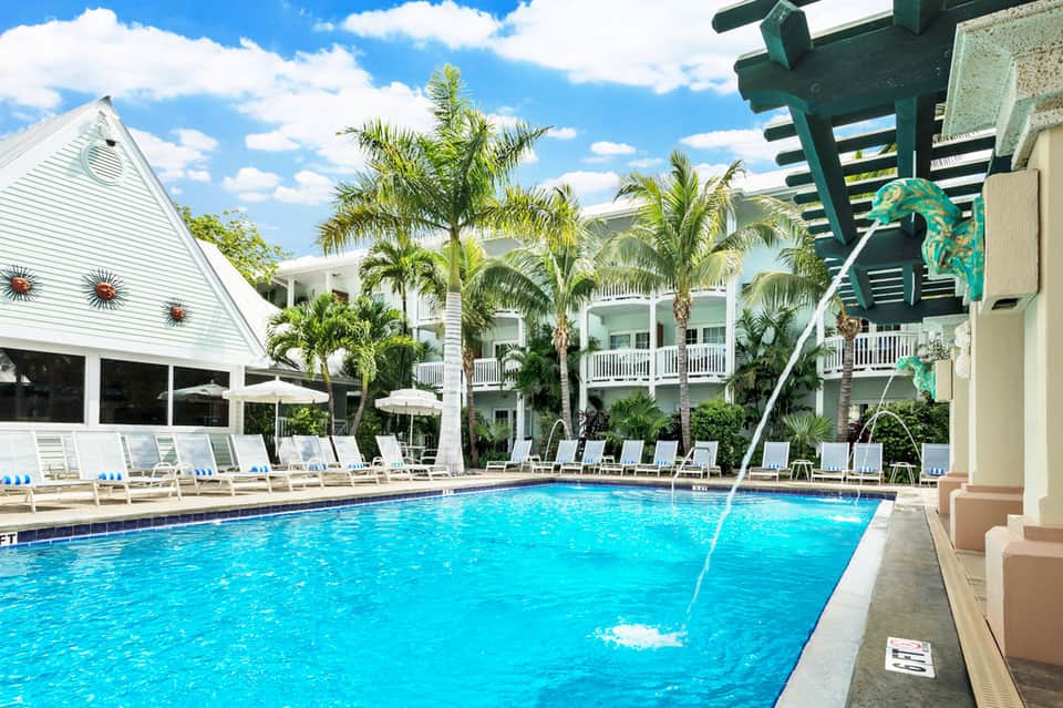 Resort pool with turquoise water, palm trees, and tropical colonial-style buildings