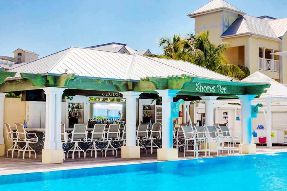 Tropical resort Shores Bar with turquoise pool, white columns, and palm trees under metal roof