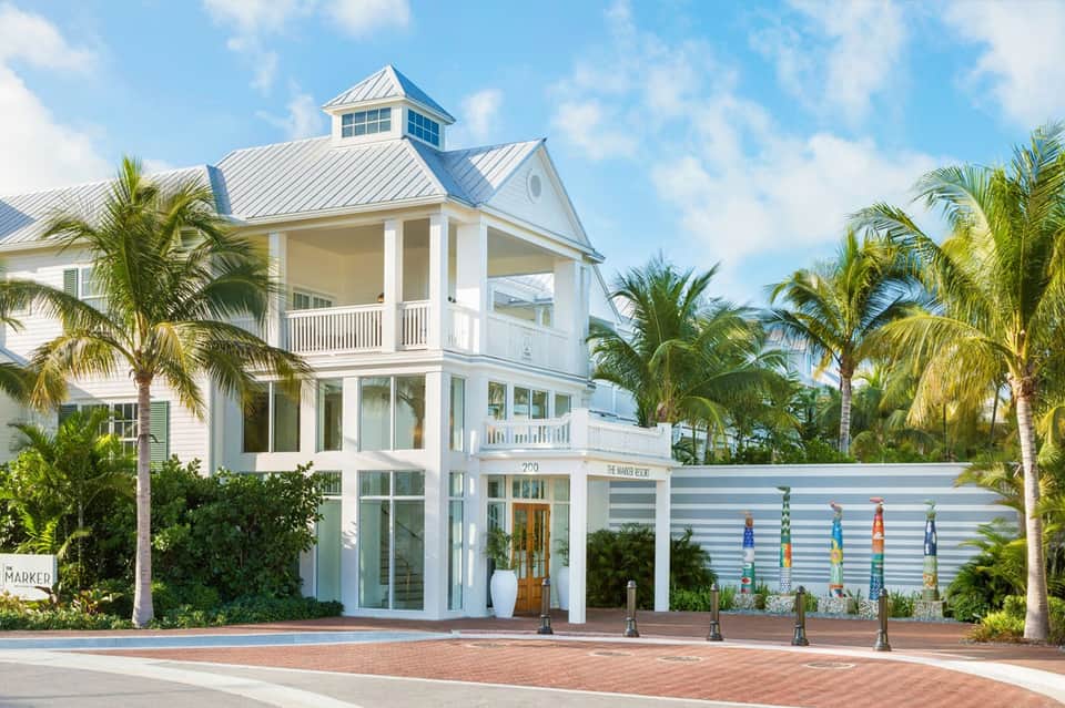 White coastal architecture building with metal roof and palm trees, colorful pole art installation