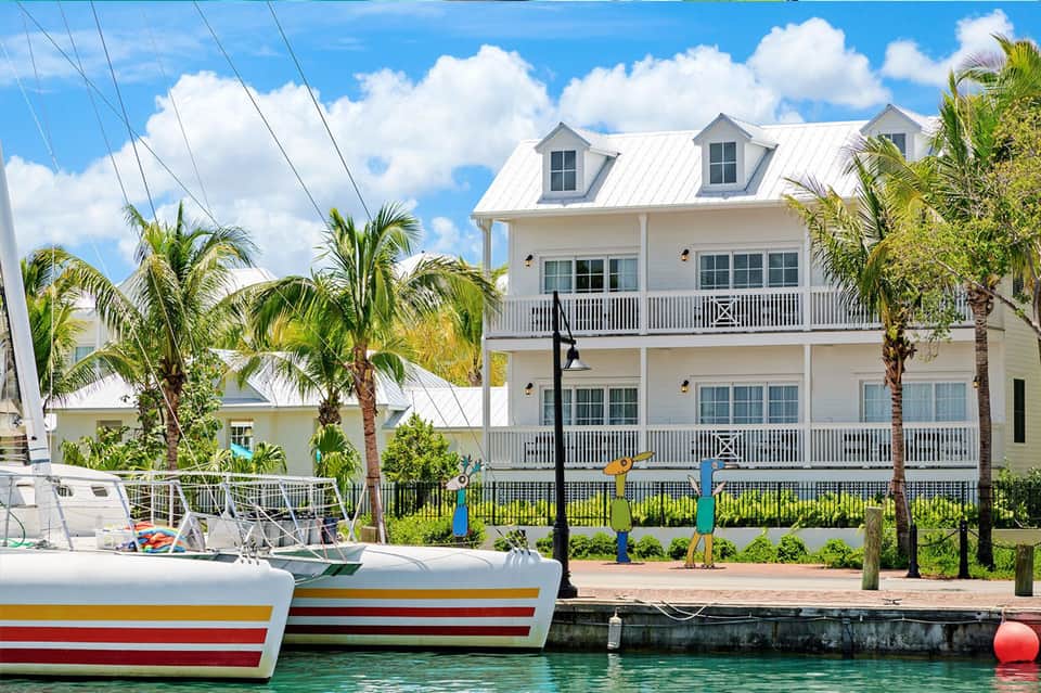Waterfront colonial-style house with white railings and metal roof docked boats in foreground