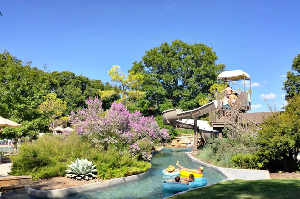 Lazy river water park with slide and tropical landscaping featuring purple flowering trees