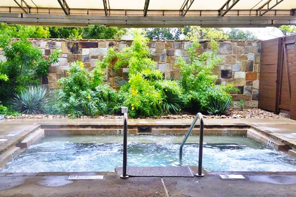 Outdoor hot spring pool with stone wall backdrop and desert landscaping under pergola