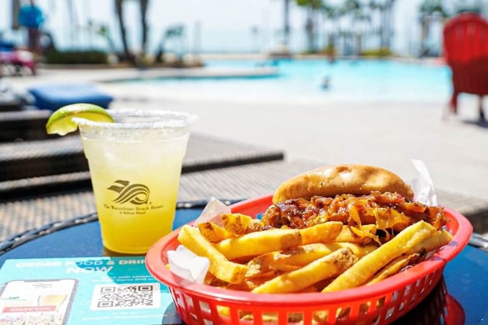 Poolside meal with cheeseburger, fries, and lemonade in a red basket by the water