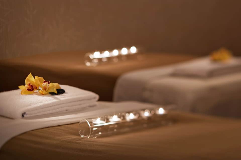 Spa setting with white rolled towels, yellow orchid flower, and lit candles on warm brown surface