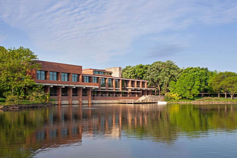 Modern brick building with large windows reflected in calm river with green trees