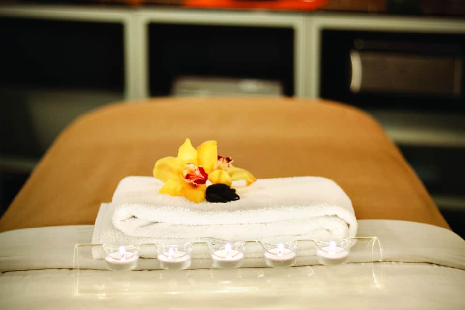 Spa treatment setup with rolled white towel, yellow orchid flower, and lit candles