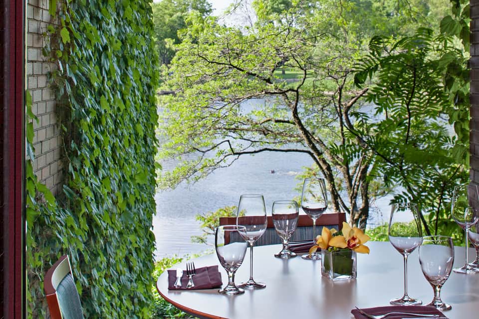 Fine dining table set with wine glasses overlooking water through ivy-covered archway