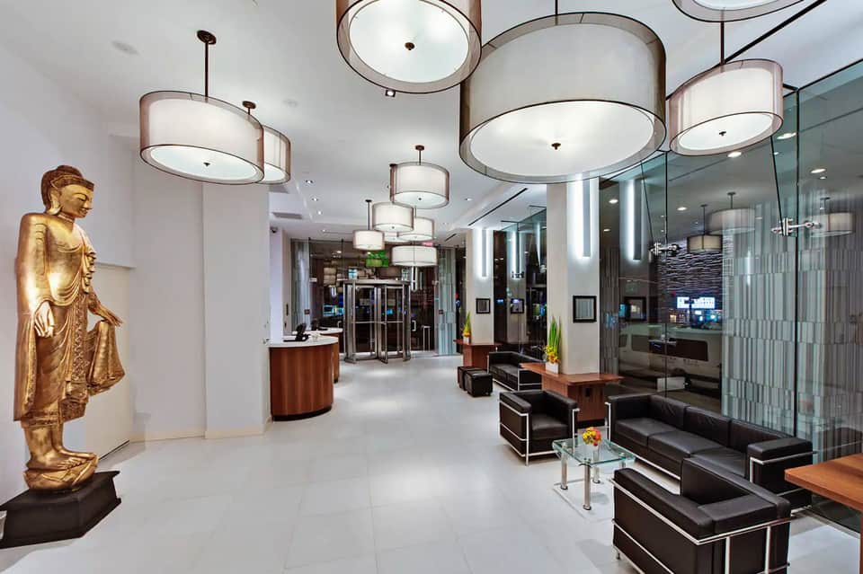 Modern hotel lobby with cylindrical pendant lights, gold Buddha statue, black seating, and glass partitions