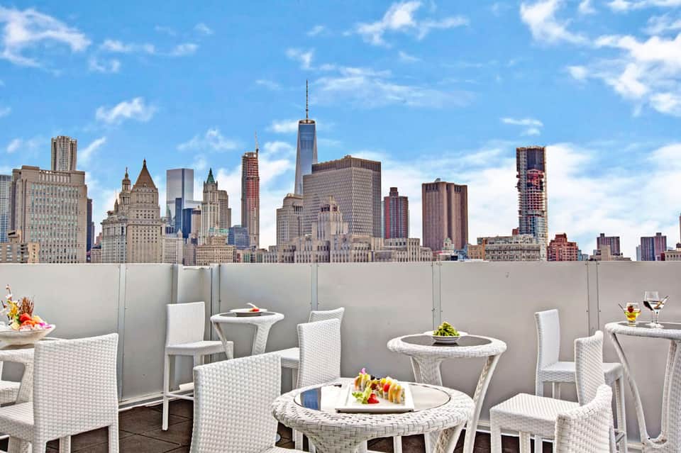 Rooftop dining area with white wicker furniture overlooking Manhattan skyline