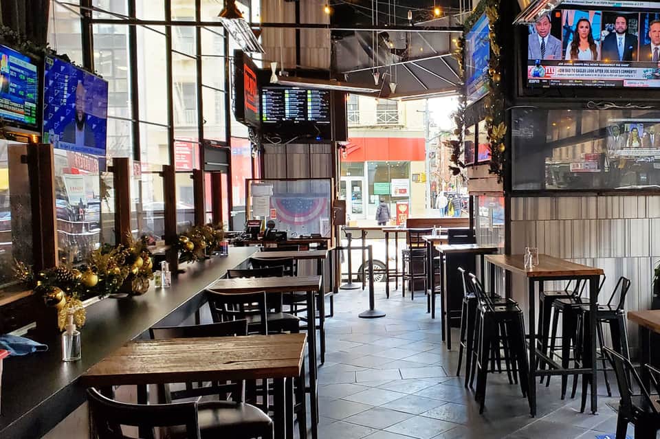Modern bar interior with black furniture, multiple TV screens, holiday decorations, and street view