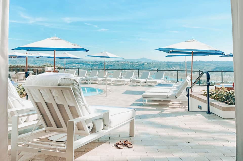 Luxury rooftop terrace with white lounge chairs, blue umbrellas, and panoramic city views