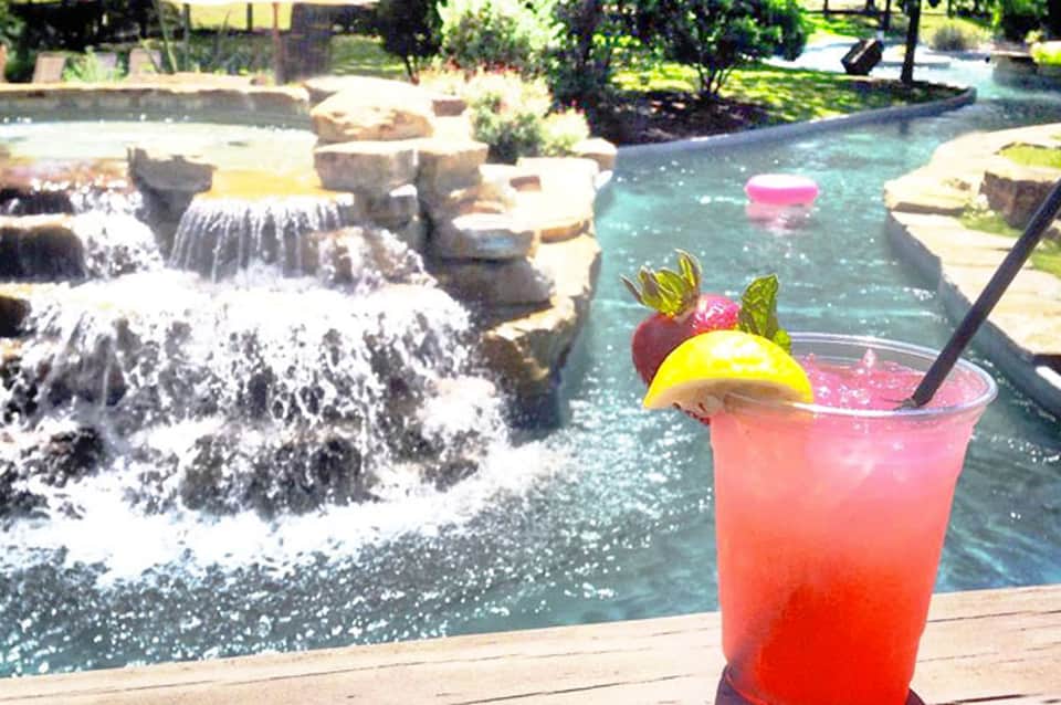 Tropical cocktail with fruit garnish overlooking turquoise lazy river with waterfall features