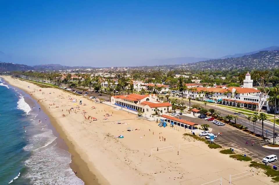 Aerial view of sandy beach with palm trees, buildings, and hills in coastal town