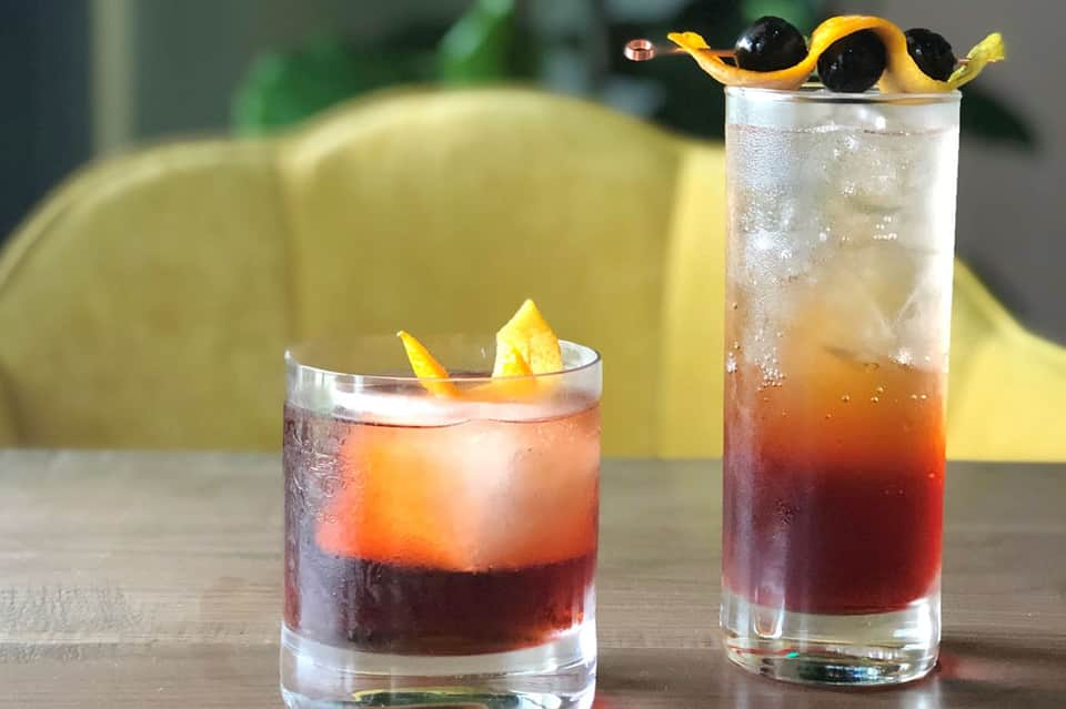 Two cocktails with dark liquid and citrus garnish on a table