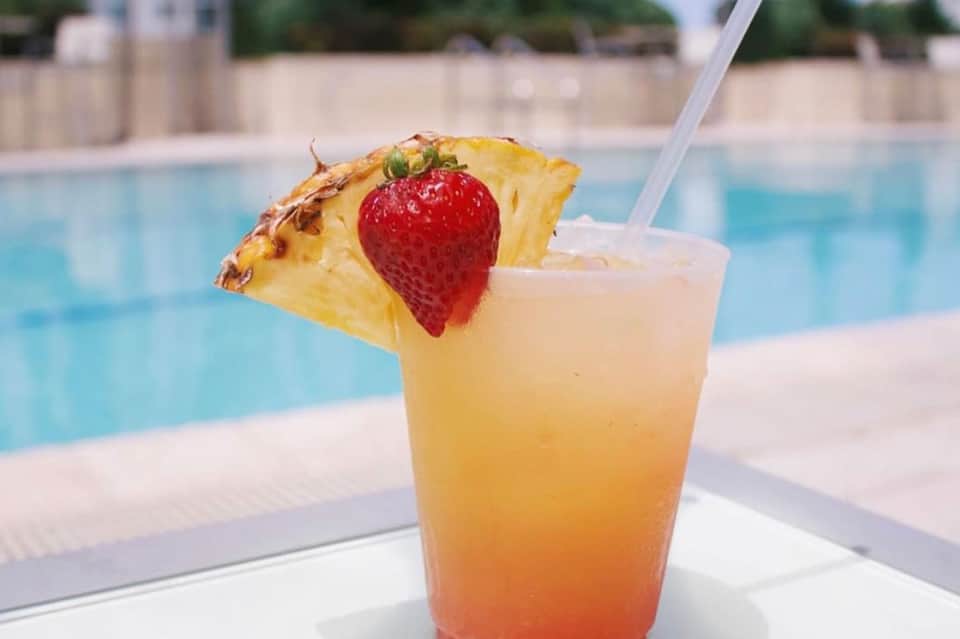 Tropical cocktail garnished with pineapple and strawberry by poolside