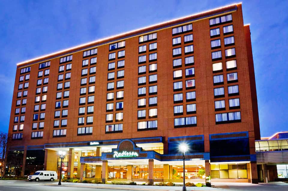 Red brick Radisson hotel exterior at dusk with lit ground-floor entrance and rows of illuminated windows