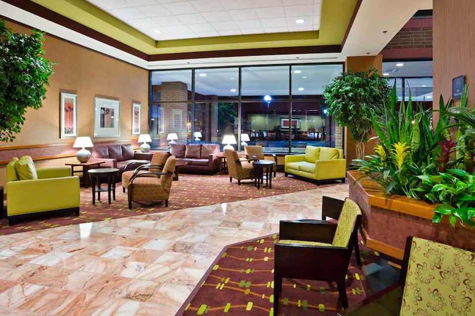 Hotel lobby with lime green ceiling, brown leather seating, marble floors, and potted plants