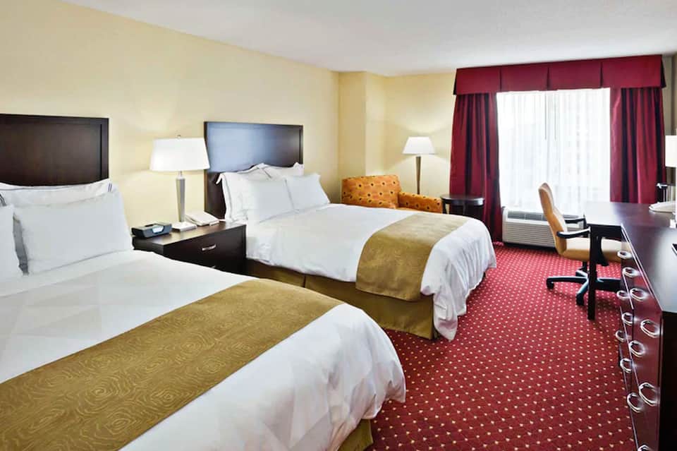 Hotel room with two queen beds, gold accents, and burgundy curtains
