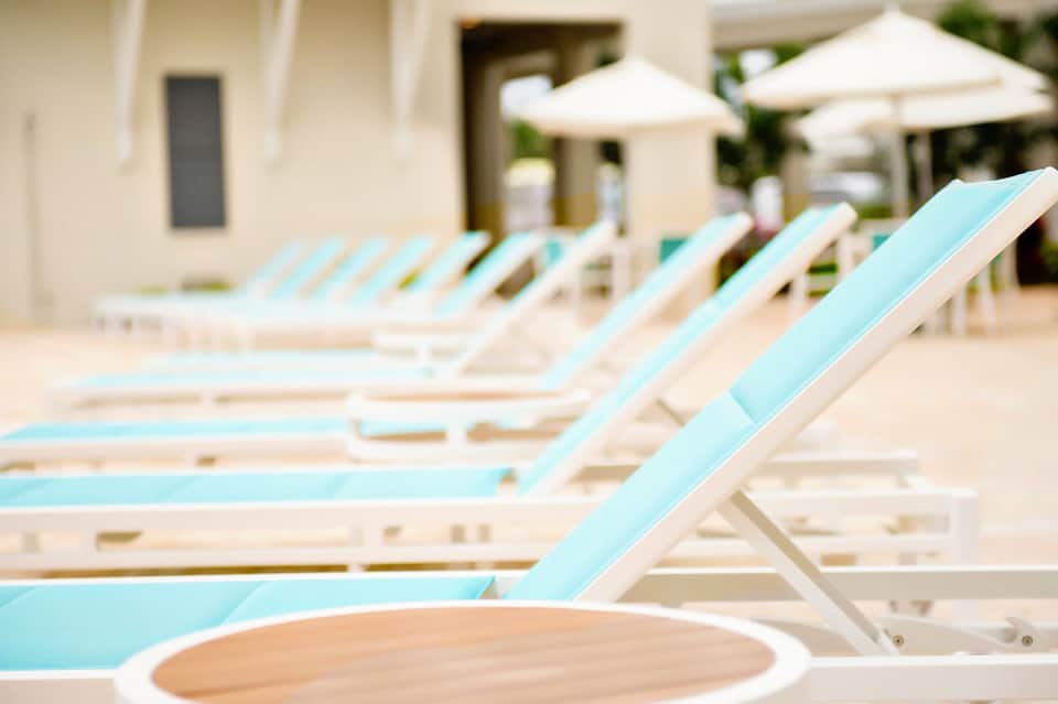 Row of turquoise and white lounge chairs with white umbrellas on a sunny resort terrace
