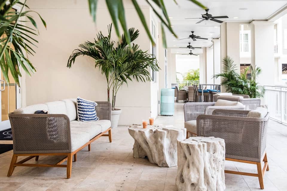 Modern covered patio with woven lounge chairs, potted palm plants, and natural stone accent tables