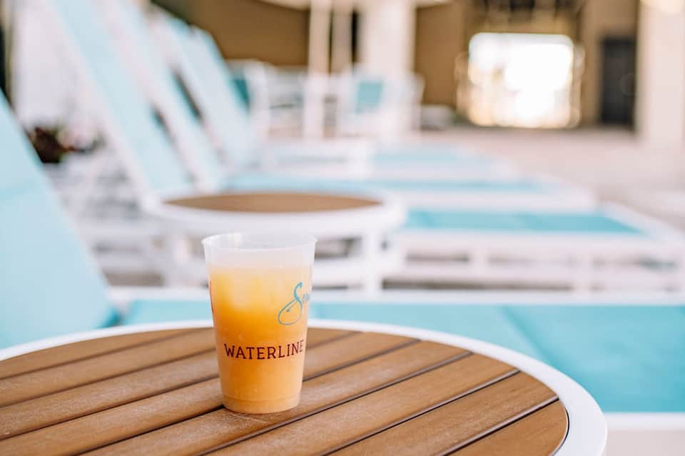Iced beverage with Waterline branding on a wooden table by a pool