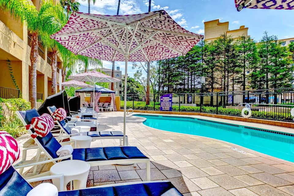 Resort pool area with pink and white umbrellas, lounge chairs, and tropical landscaping