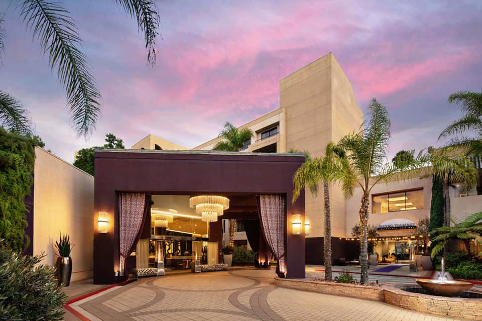 Modern resort entrance at dusk with illuminated chandelier and palm trees