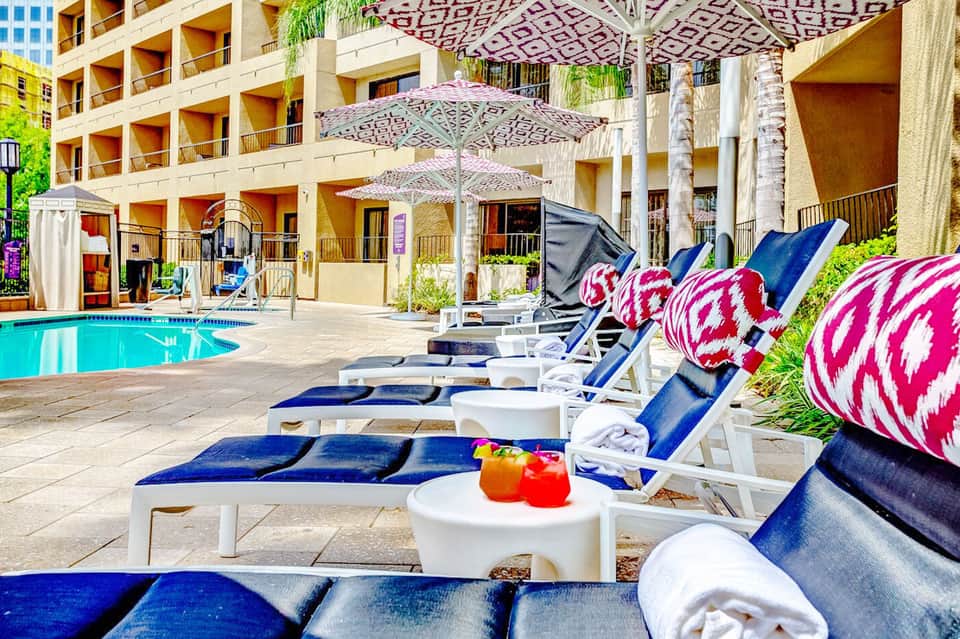 Resort poolside with lounge chairs, patterned umbrellas, and multi-story building backdrop