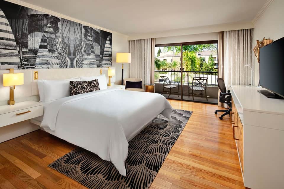 Modern hotel bedroom with king bed, balcony view of palm trees, and contemporary decor