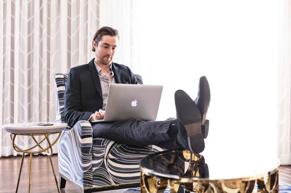 Man in business casual attire working on laptop while relaxing in striped chair with feet up